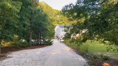 Wide gravel driveway running between woodland toward the buildings
