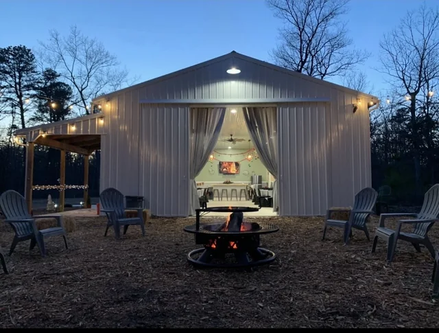 Event building lit at twilight, with an open fire pit and seating on the gravel apron in front of it