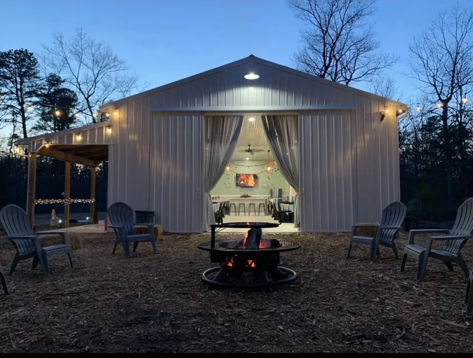 Event building lit at twilight, with an open fire pit and seating on the gravel apron in front of it